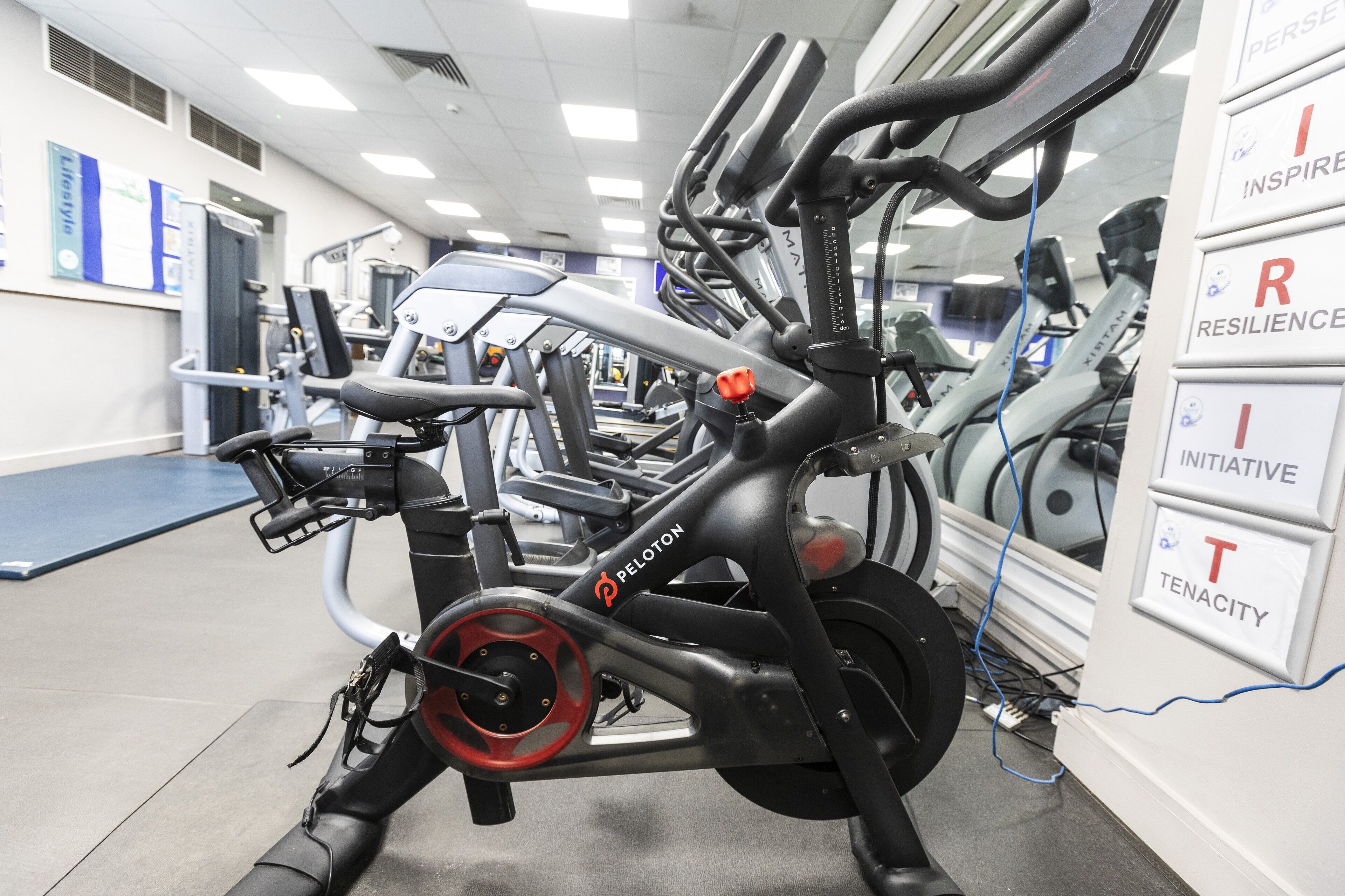 A gym with exercise equipment, including a Peloton bike, and motivational posters on the wall.