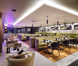 A restaurant with multiple dining areas, including booths and tables, with a modern interior design and a view of the cityscape.