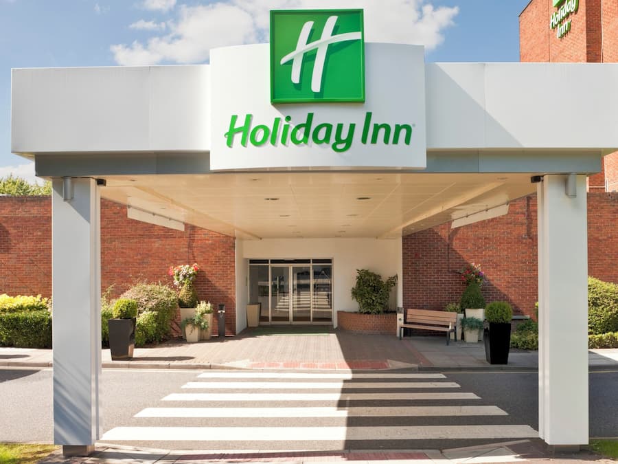 L’entrée d’un hôtel Holiday Inn, avec un chemin dégagé menant aux portes, entourée de murs en briques et de plantes en pot.