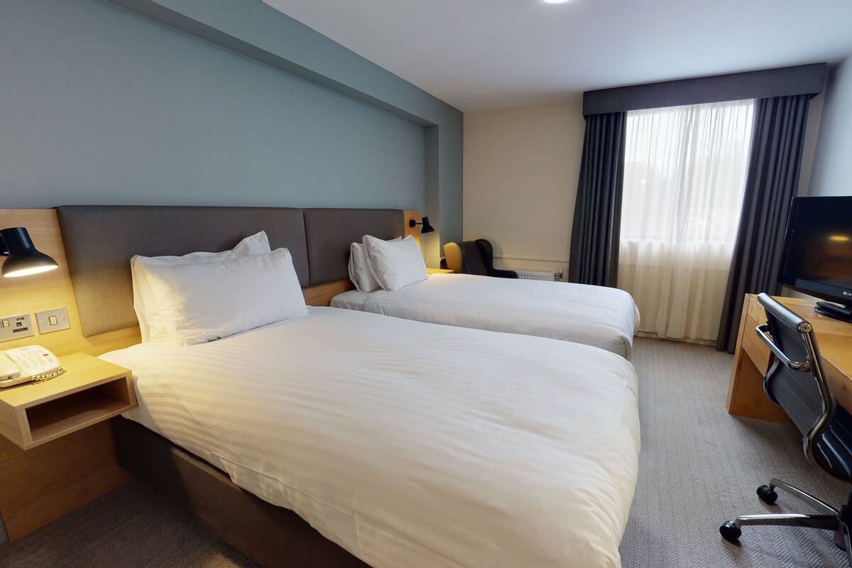 Une chambre d’hôtel avec deux lits, un bureau avec une télévision, une chaise et une lampe.
