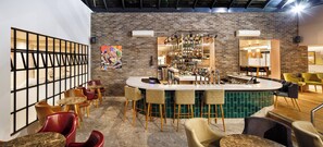Ein Barbereich mit Backsteinwand, Barhocker, einer Theke mit Zapfhähnen und einer Sitzecke mit Stühlen und Tischen.