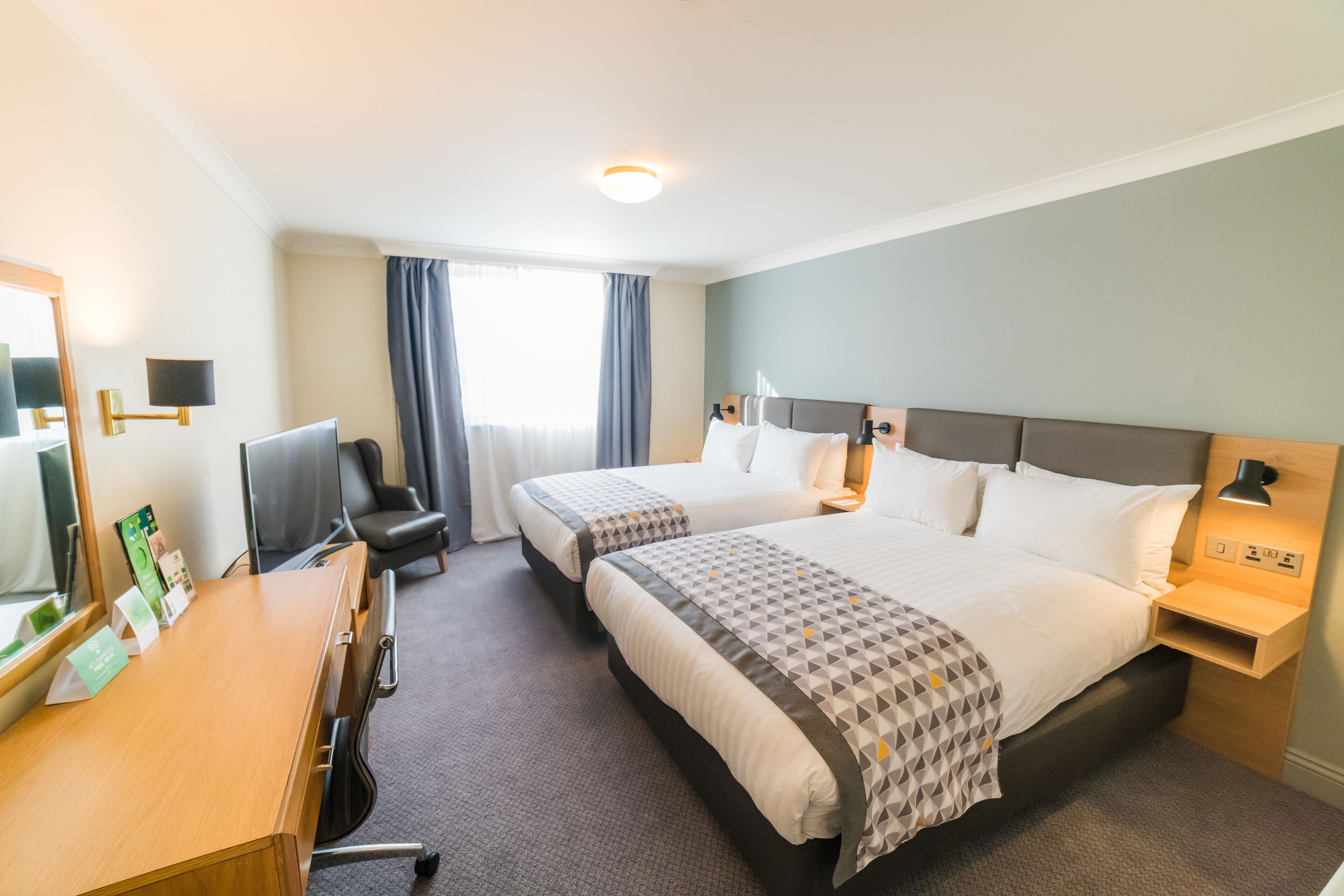 Ein Hotelzimmer mit zwei Betten, einem Schreibtisch, einem Stuhl, einem Nachttisch und einem Spiegel.