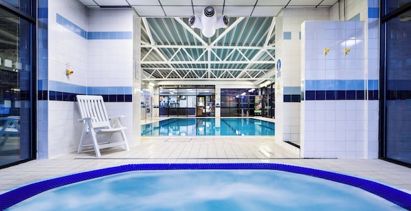 An indoor swimming pool with a clear view of the pool area, a white chair, and a tiled wall with a blue stripe.