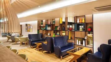 A modern interior with a wooden floor, leather armchairs, a wooden coffee table, and a bookshelf with various decorative items.