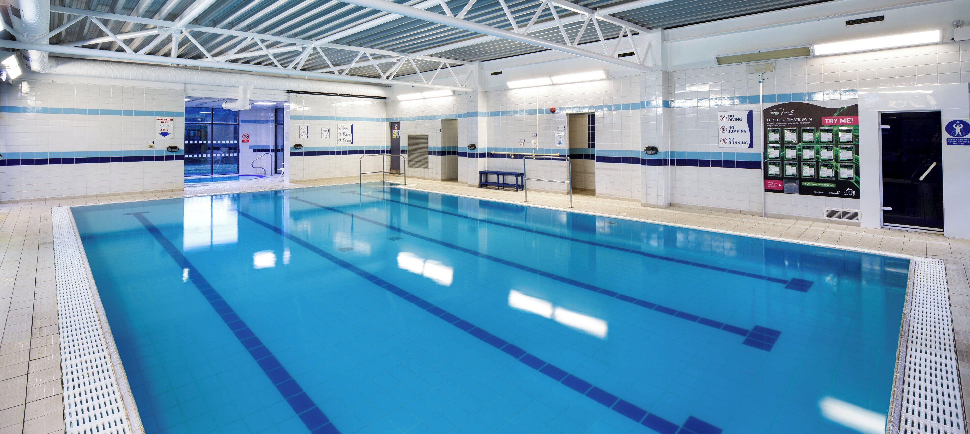 Una piscina interior con carriles delimitados, zona de trampolín y vestuario.