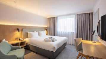 Une chambre d’hôtel avec un grand lit, un bureau, une chaise, une télévision et une fenêtre avec des rideaux.