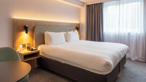 Une chambre d’hôtel avec un grand lit, des tables de chevet, un bureau et une fenêtre avec des rideaux.