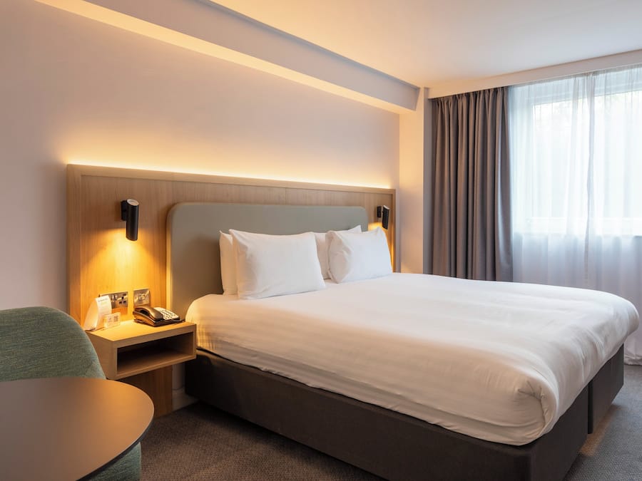 A hotel room with a large bed, bedside tables, a desk, and a window with curtains.