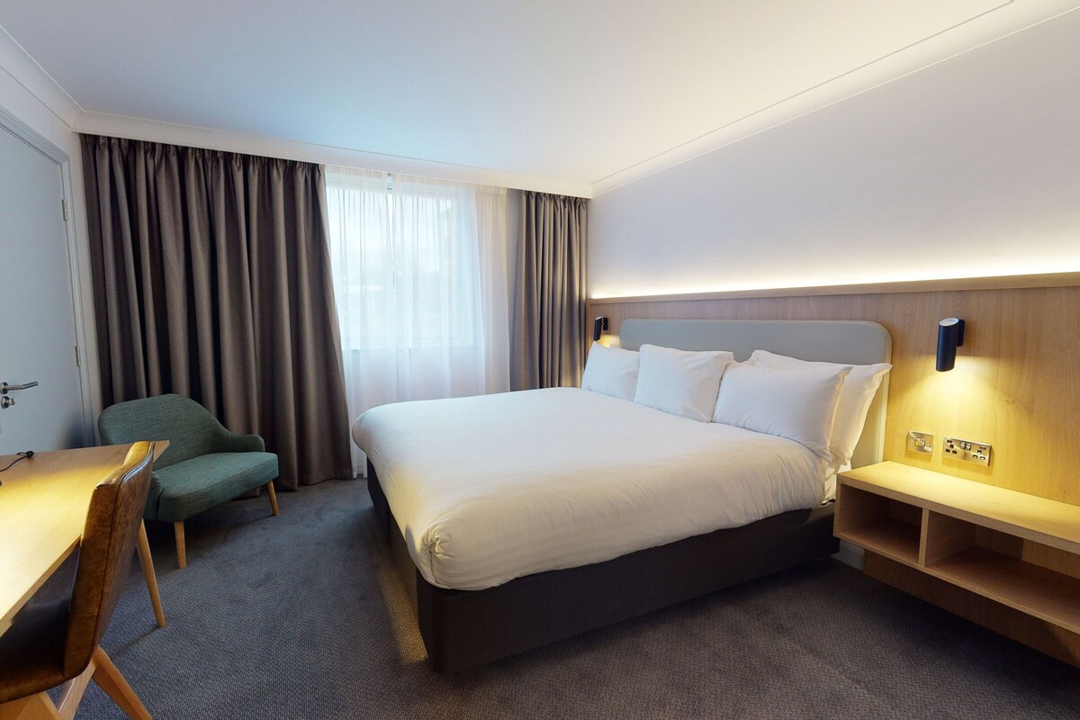 Une chambre d’hôtel avec un lit, un bureau, une chaise et une petite table avec une lampe.