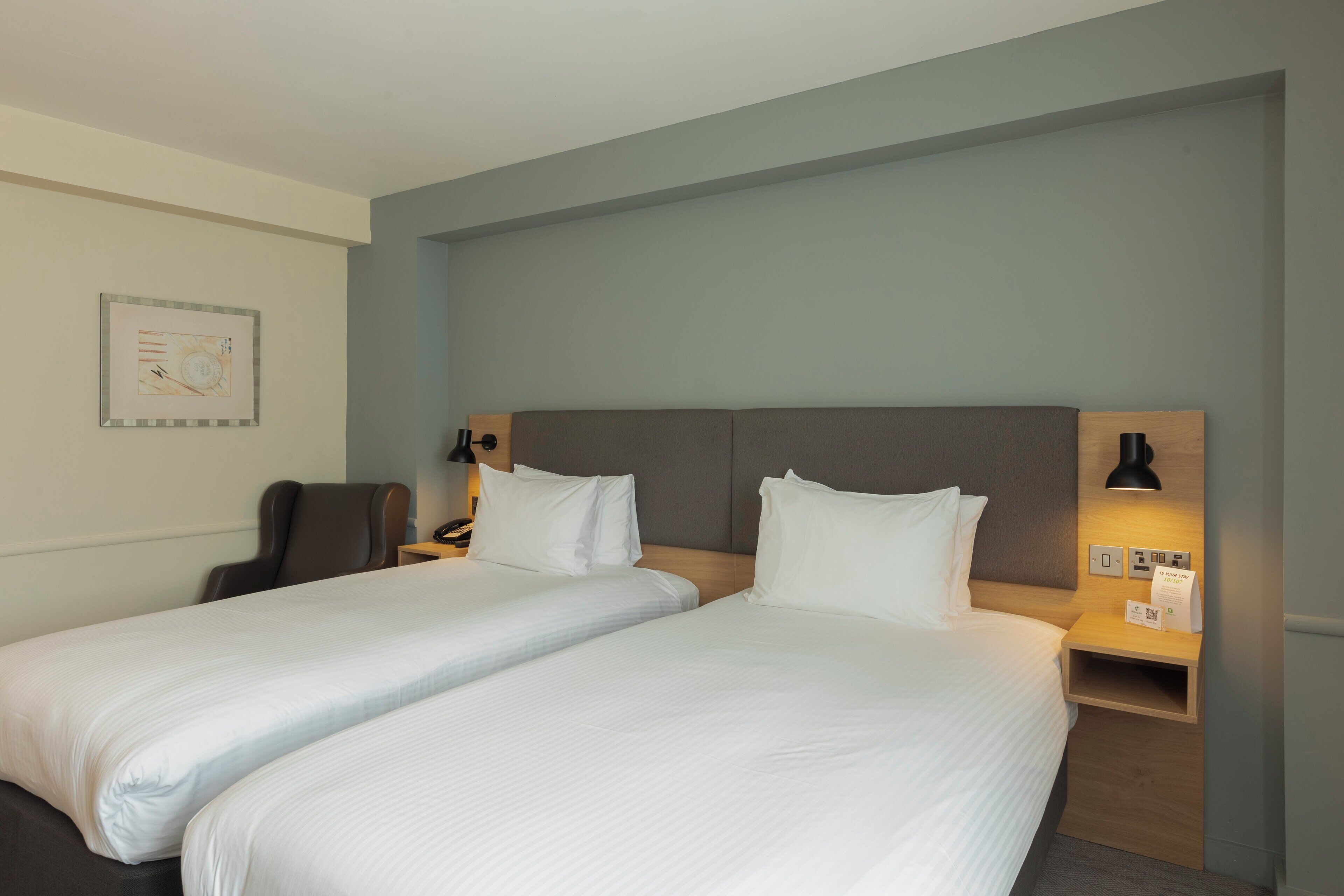 Hotelkamer met twee bedden, een bureau, een stoel, een lamp en een wandplank met een bordje.