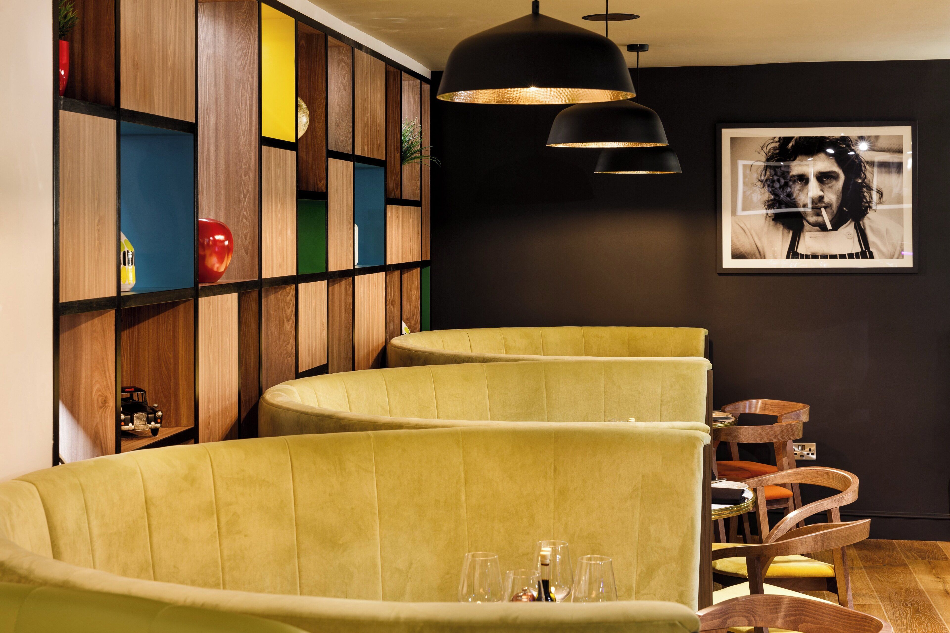 A modern interior with curved yellow seating, wooden panel walls, and a black pendant light.