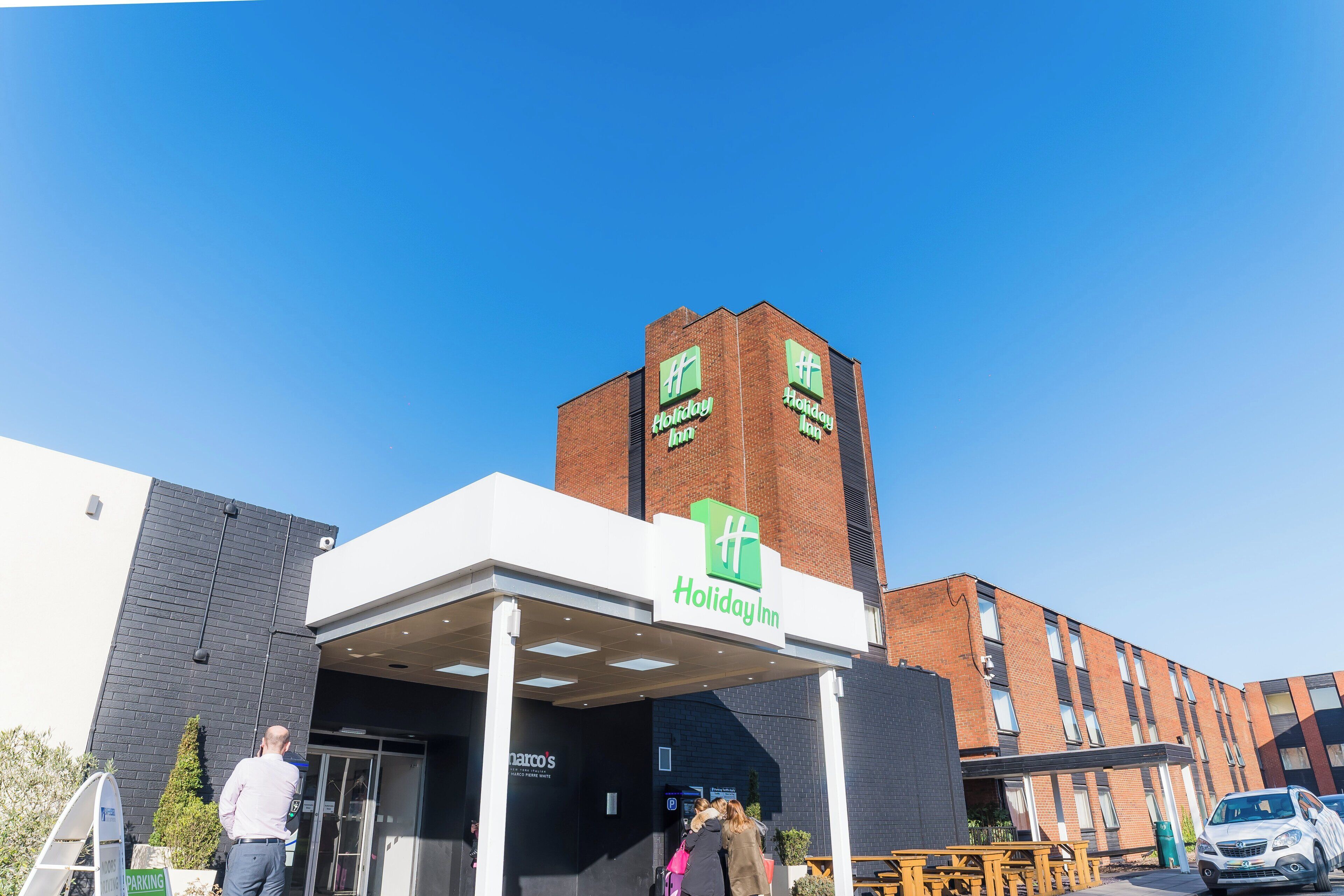 Et Holiday Inn hotel med en moderne murstensfacade og en overdækket indgang.