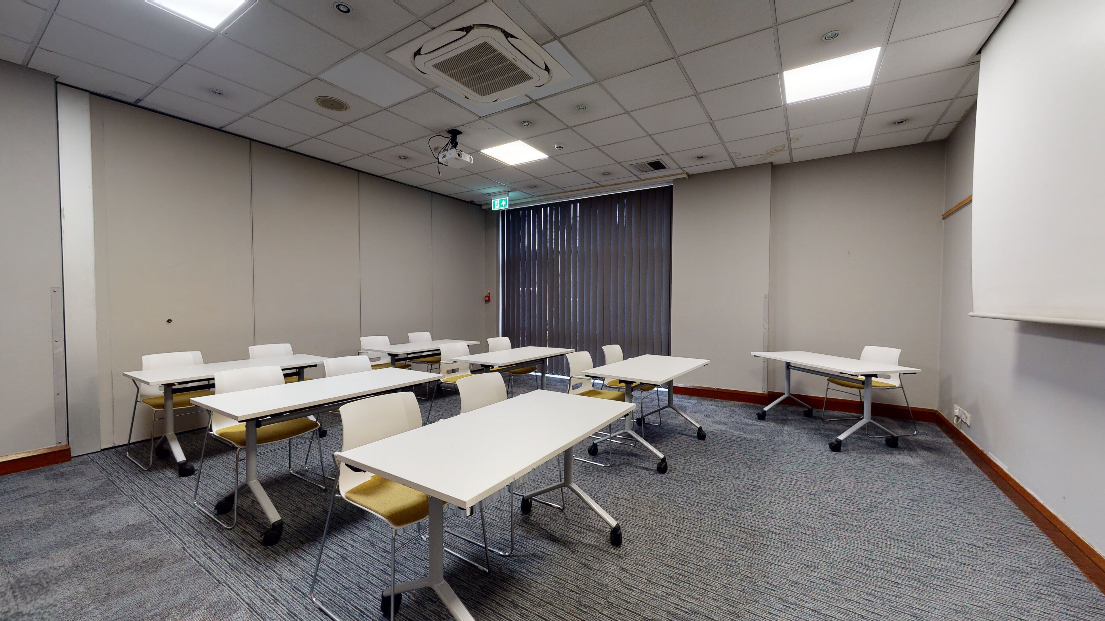 A conference room with white tables and chairs, carpeted floor, and a projector screen.