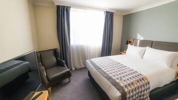 A hotel room with a bed, a chair, a desk, a TV, and a window with curtains.