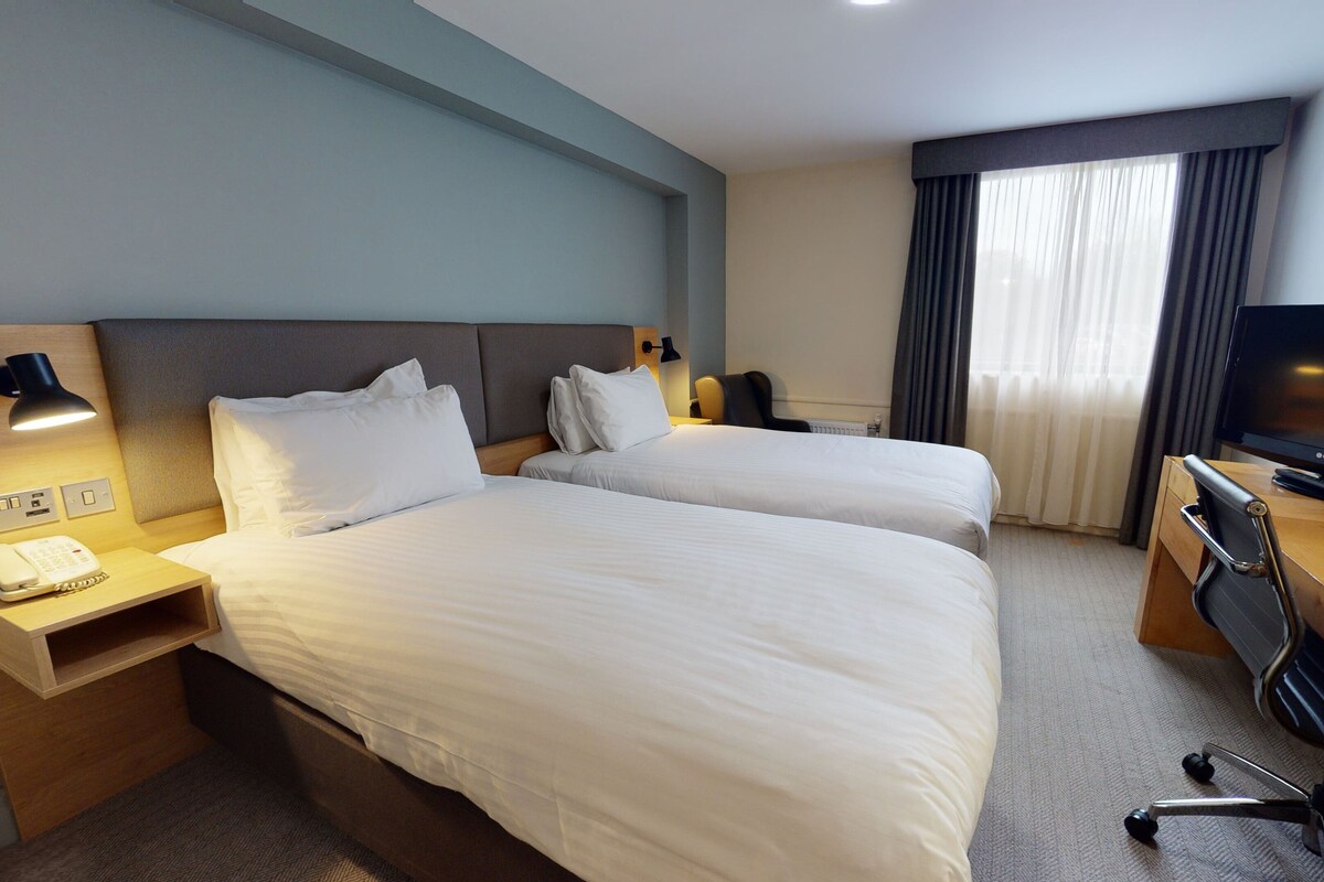Une chambre d’hôtel avec deux lits, un bureau avec une télévision, une chaise et une lampe.