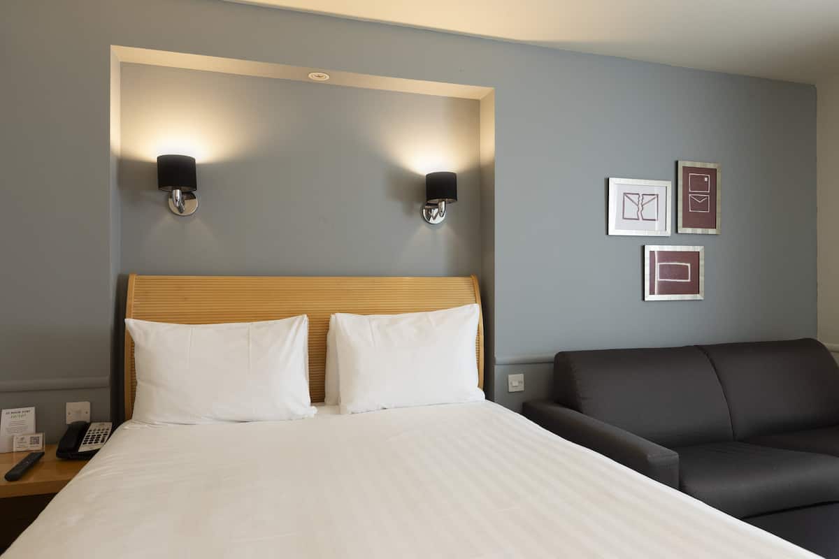 Une chambre d’hôtel avec un lit, deux lampes de chevet, une table de chevet avec un téléphone et un canapé en cuir foncé.