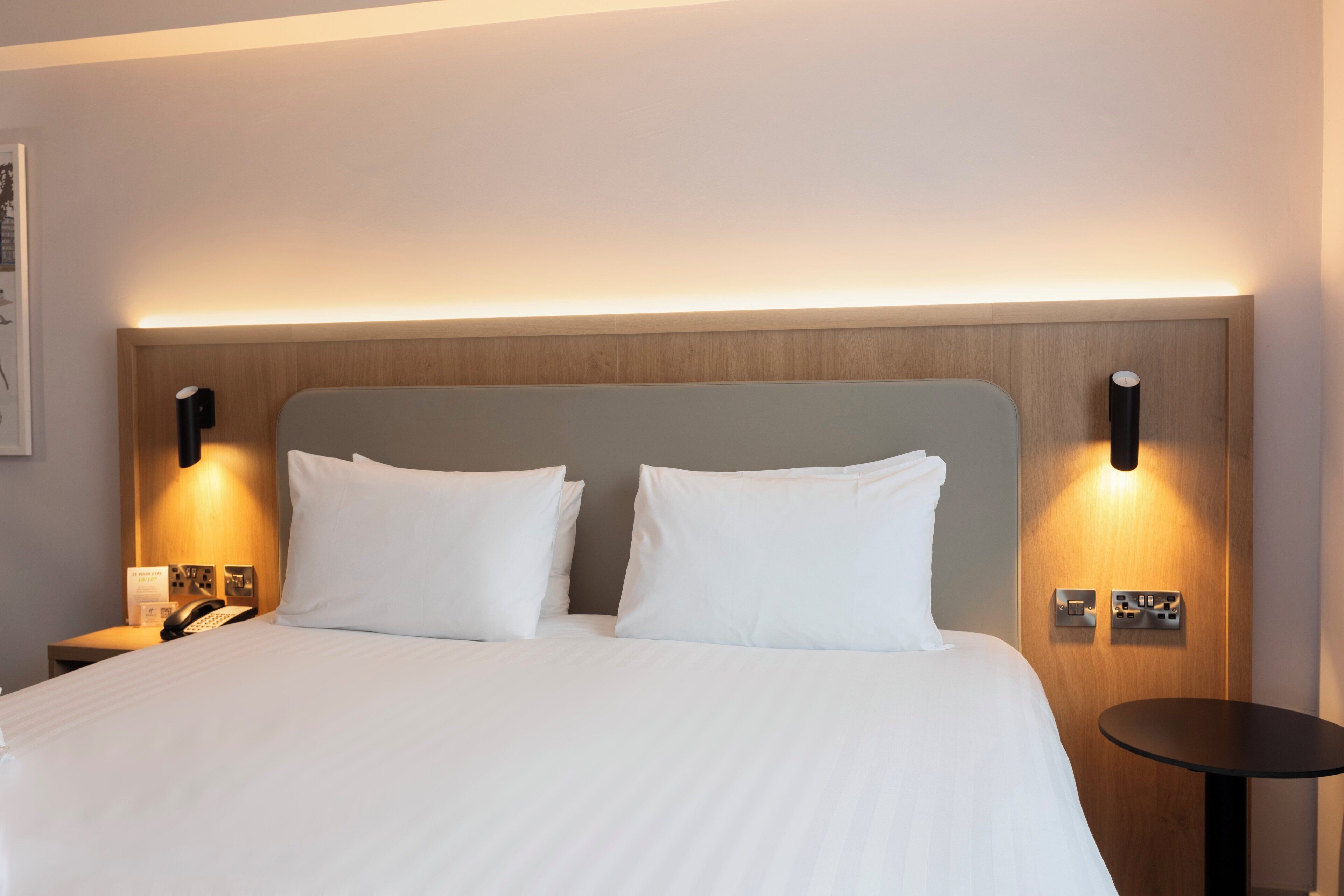 Une chambre d’hôtel avec un grand lit, deux tables de chevet, un téléphone sur la table de chevet et une petite table ronde.