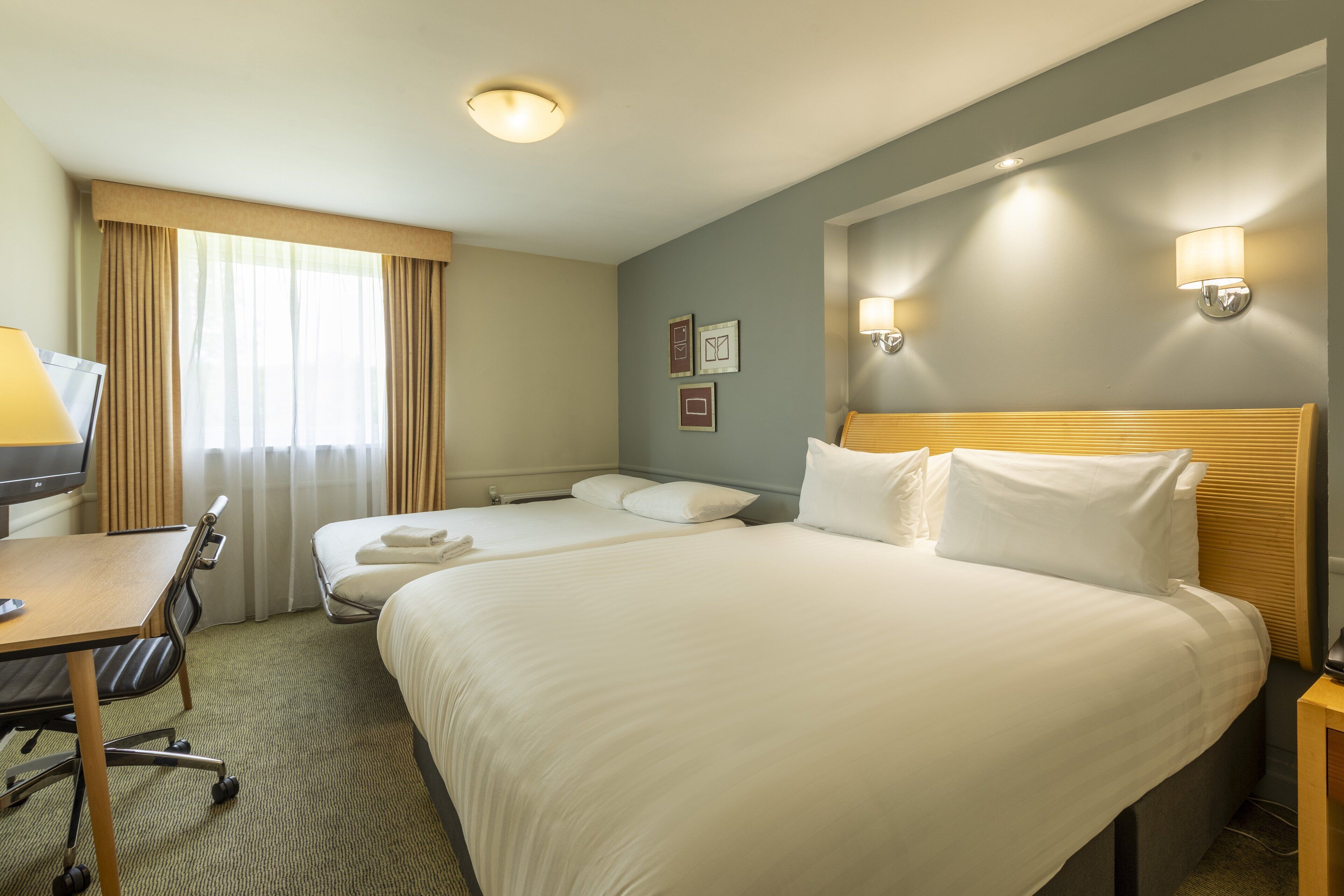 A hotel room with two beds, a desk, and a chair.
