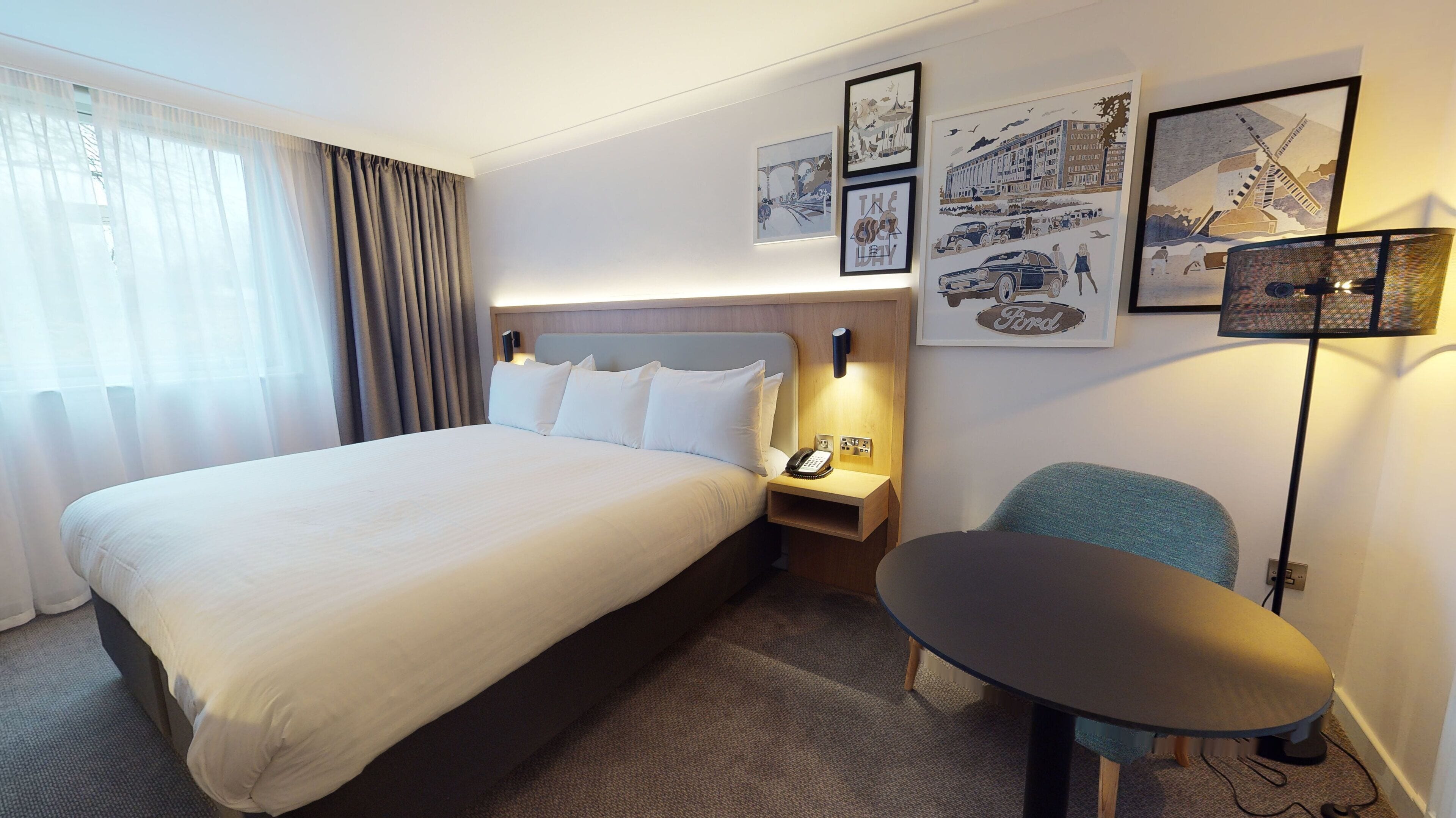 Una habitación de hotel con una cama grande, una mesita de noche con lámpara, una silla y una obra de arte en la pared.