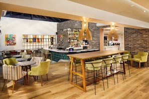 A bar area with a wooden bar counter, multiple seating options including bar stools and chairs, and a variety of bottles and glasses on shelves.