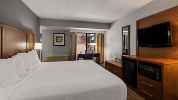 A hotel room with a large bed, a desk with a chair, a television, and a microwave.