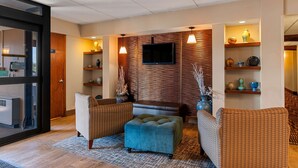 A modern living room with a flat-screen TV, wicker sofas, a blue ottoman, and wooden paneling. - Best Western Bridgeview Hotel (Superior)