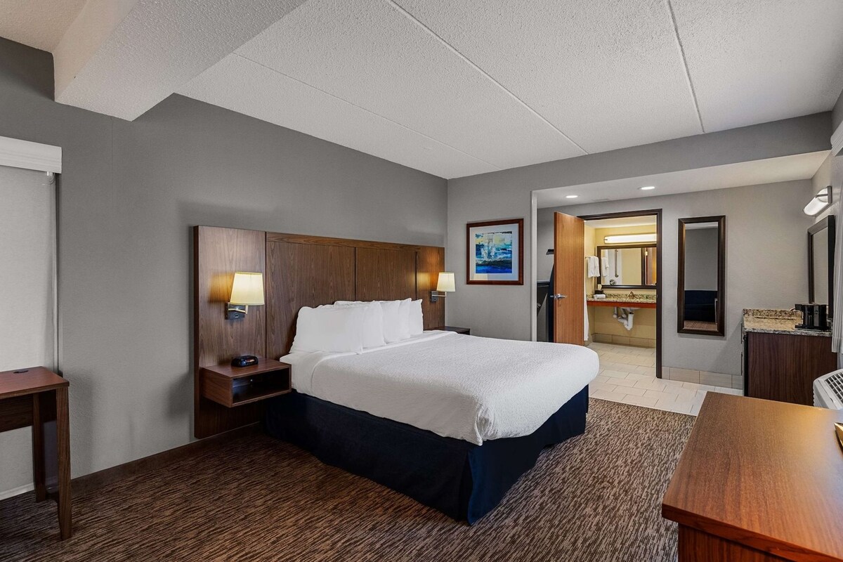 A hotel room with a large bed, bedside tables, a desk, and a bathroom visible through an open door.