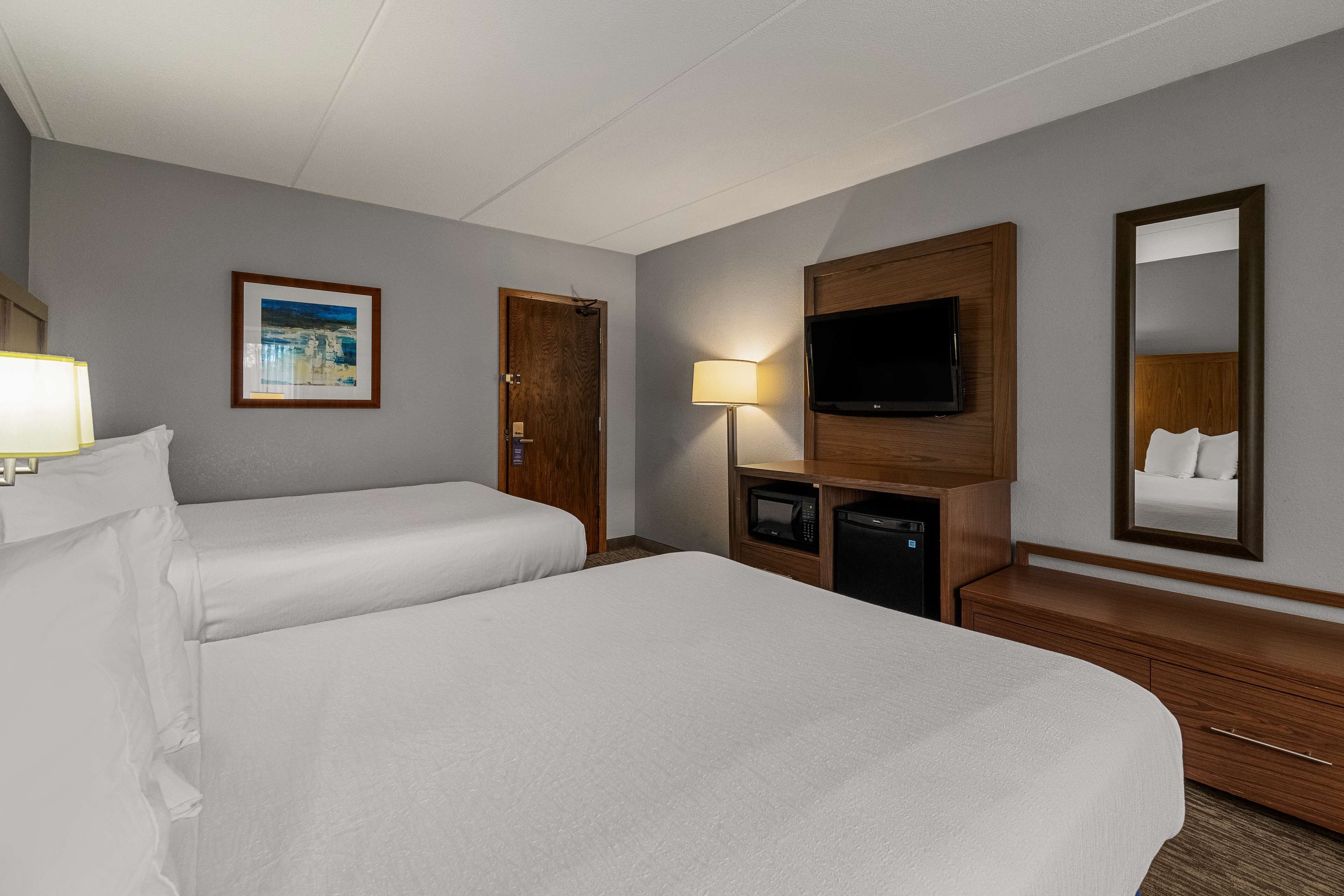 Habitación de hotel con dos camas, televisión, lámpara y espejo.