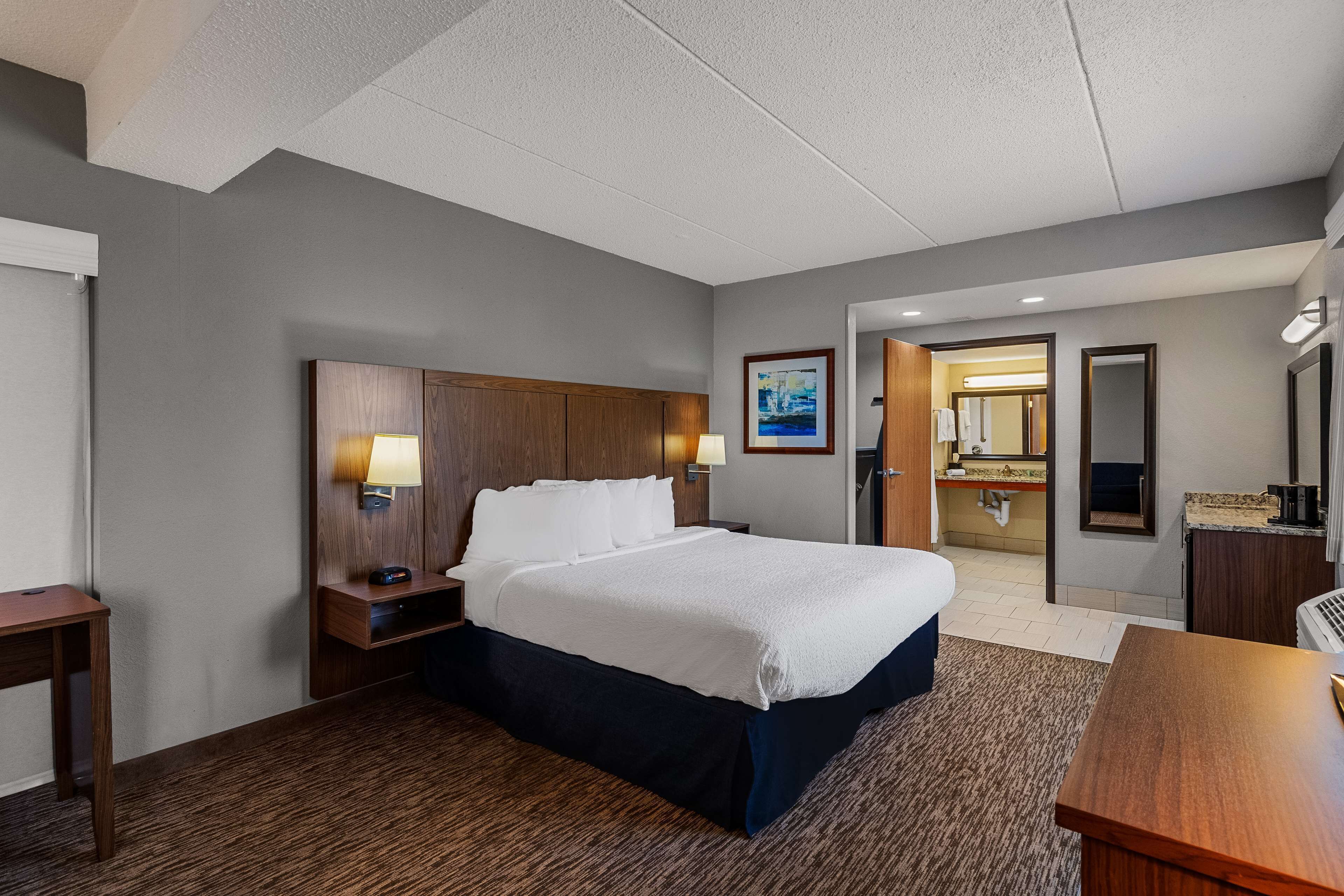 A hotel room with a large bed, a desk, a nightstand, and a bathroom visible through an open door.