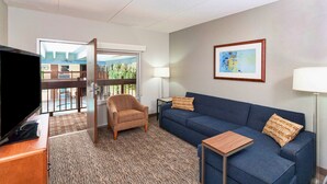 A hotel room with a television, a blue sofa, a brown armchair, a small wooden table, and a framed abstract painting on the wall. - Best Western Bridgeview Hotel (Superior)