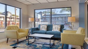Un salon moderne comprenant un canapé, deux fauteuils, une table basse et des lampes. De grandes fenêtres offrent une vue sur un immeuble doté de balcons.