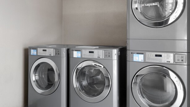 A row of three stacked front-loading washing machines in a commercial setting.