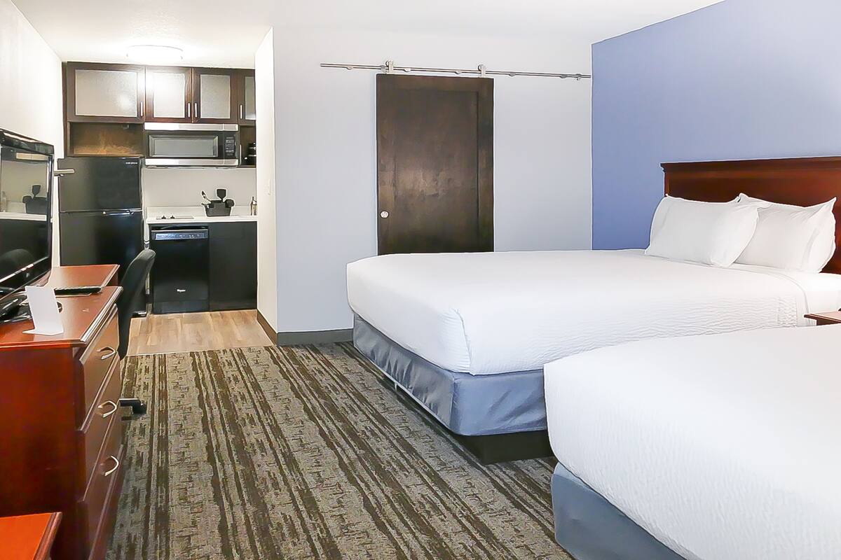 Une chambre d’hôtel avec deux lits, un bureau avec un ordinateur, un four à micro-ondes et une petite kitchenette.