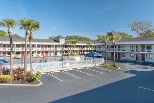 A motel with multiple-story buildings, a parking lot, and palm trees.