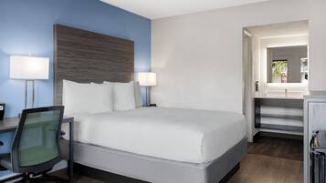 A hotel room with a bed, desk, chair, and a view of the outside.