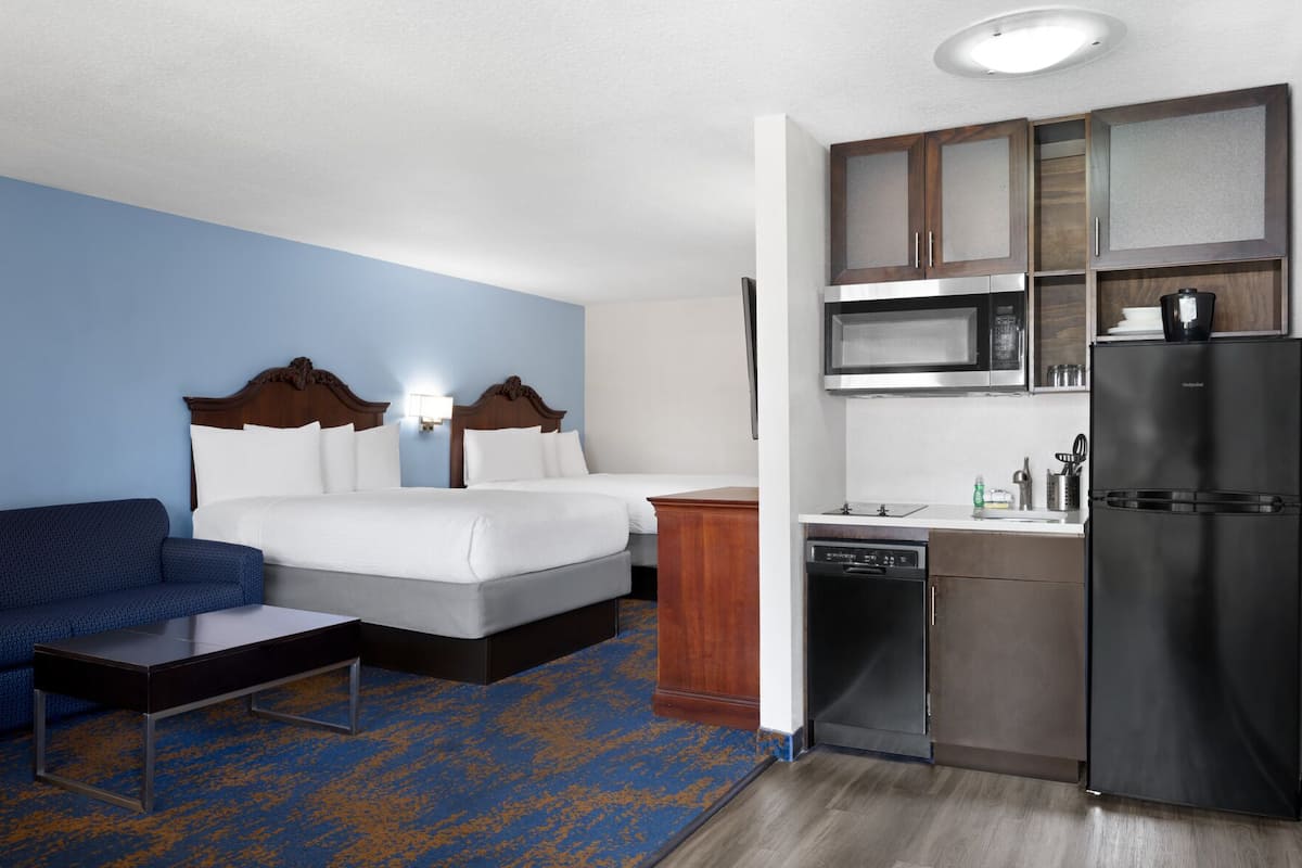 Une chambre d’hôtel avec un lit, un canapé, une kitchenette et une moquette bleue.