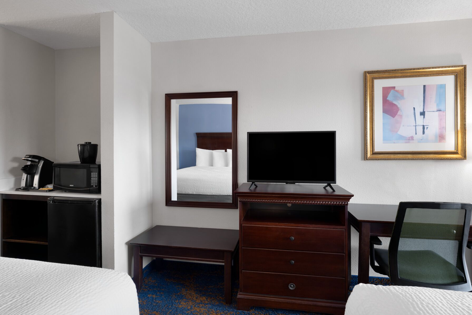A hotel room with a bed, a desk with a coffee maker, a television, a dresser, and a chair.