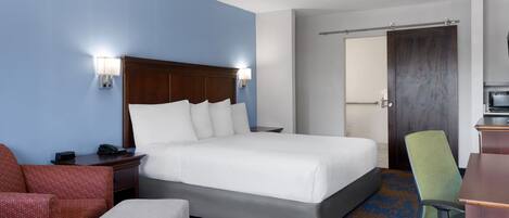 A hotel room with a large bed, a desk with a chair, a small couch, and a bathroom door.