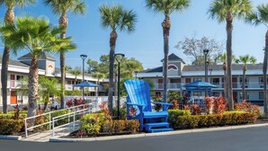 A hotel with a pool area, palm trees, and a blue Adirondack chair.