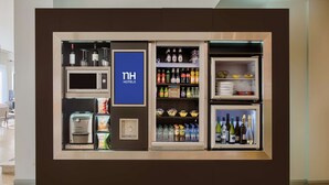 Un minibar con microondas, cafetera y una selección de bebidas y aperitivos.
