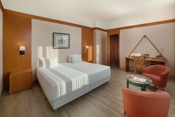 Una habitación de hotel con una cama grande, un escritorio, una silla y una mesita.