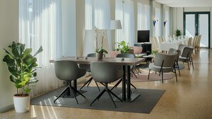 A modern conference room with a long table, chairs, a TV, and potted plants.