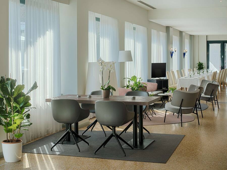 Uma sala de conferências moderna com uma mesa comprida, cadeiras, uma TV e plantas em vasos.