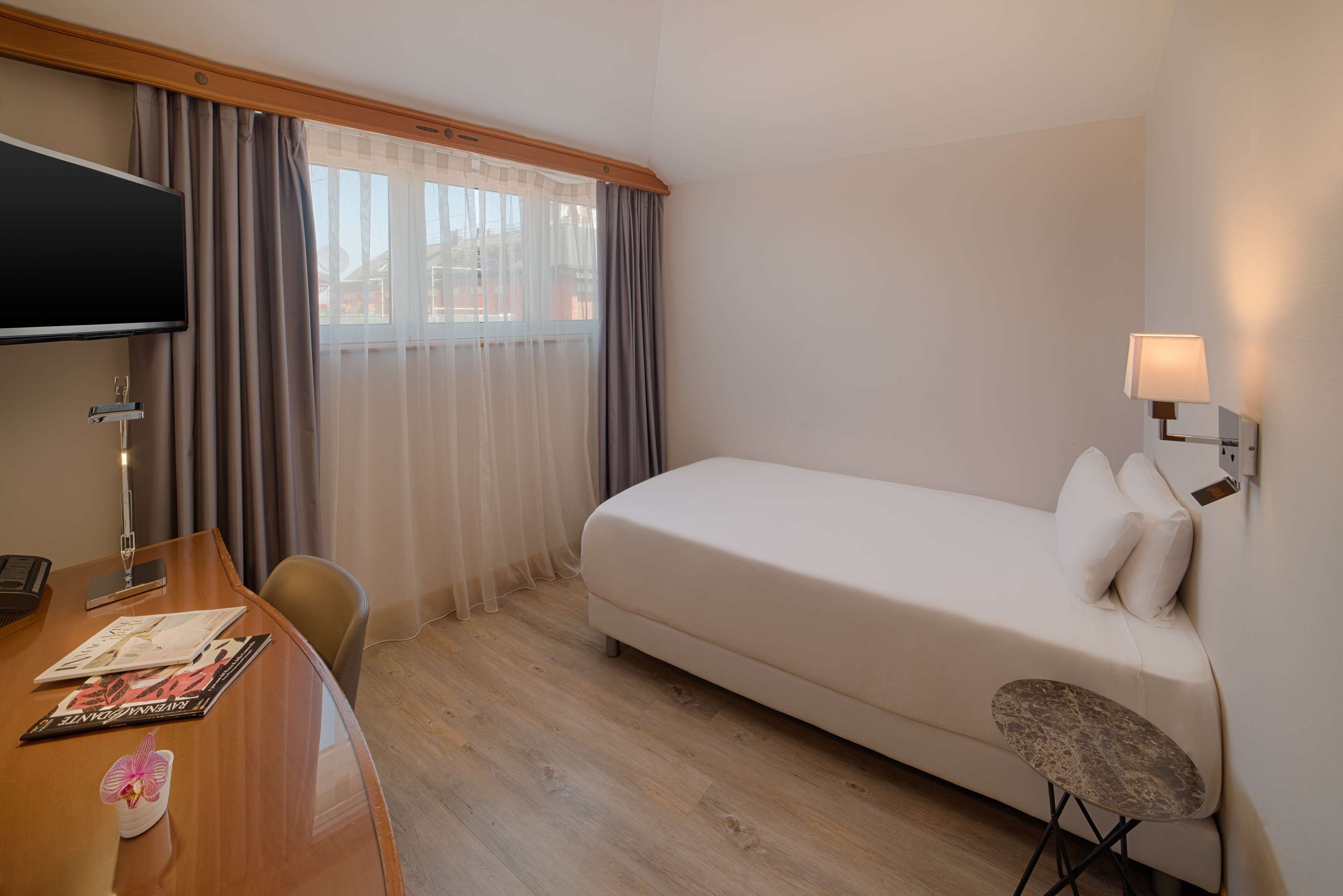 Una habitación de hotel con cama, escritorio con computadora, silla, mesita y televisor.