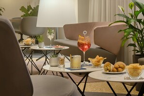 Un área de descanso moderna con asientos, una mesa con aperitivos y bebidas, y una planta en maceta.