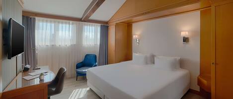 A hotel room with a large bed, a desk with a computer, a chair, and a television.