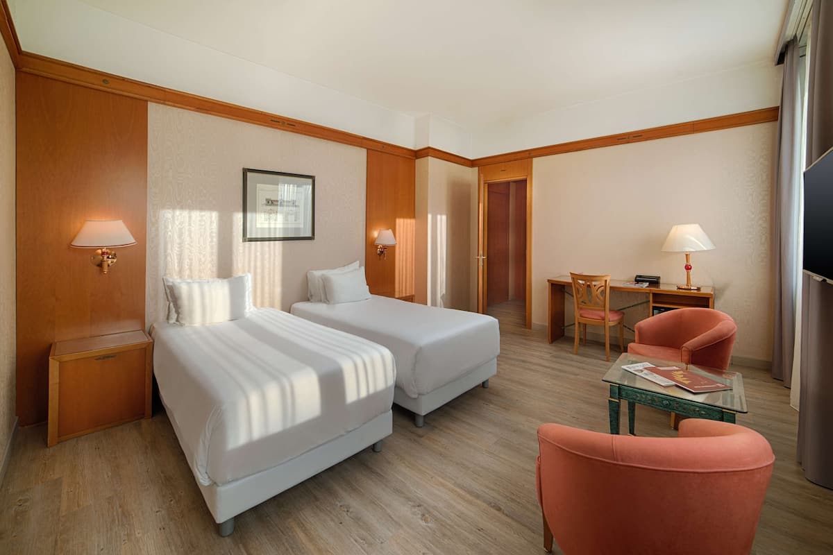 A hotel room with two beds, a desk, a chair, and a TV.