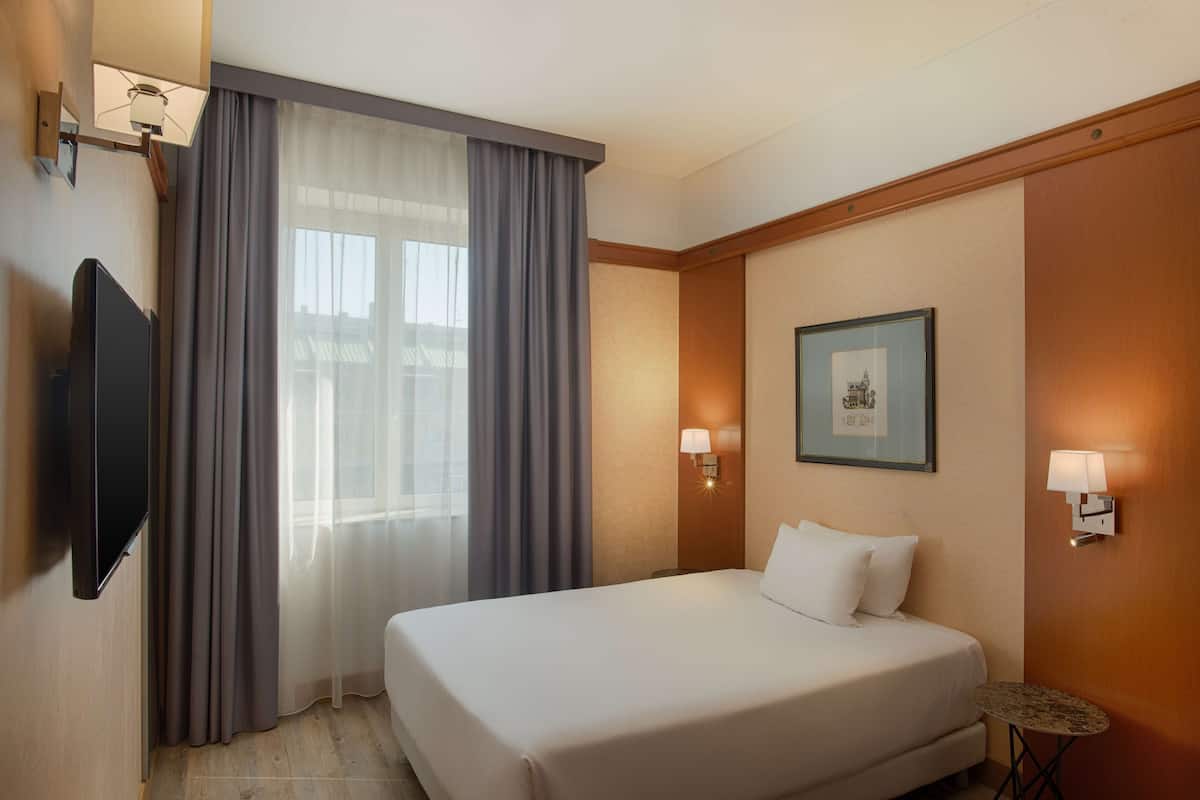 A hotel room with a bed, a TV, a small table, and a framed picture on the wall.