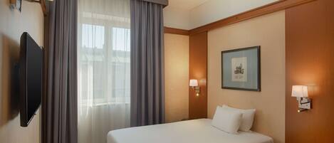 Una habitación de hotel con una cama, un televisor, una mesita pequeña y un cuadro en la pared.