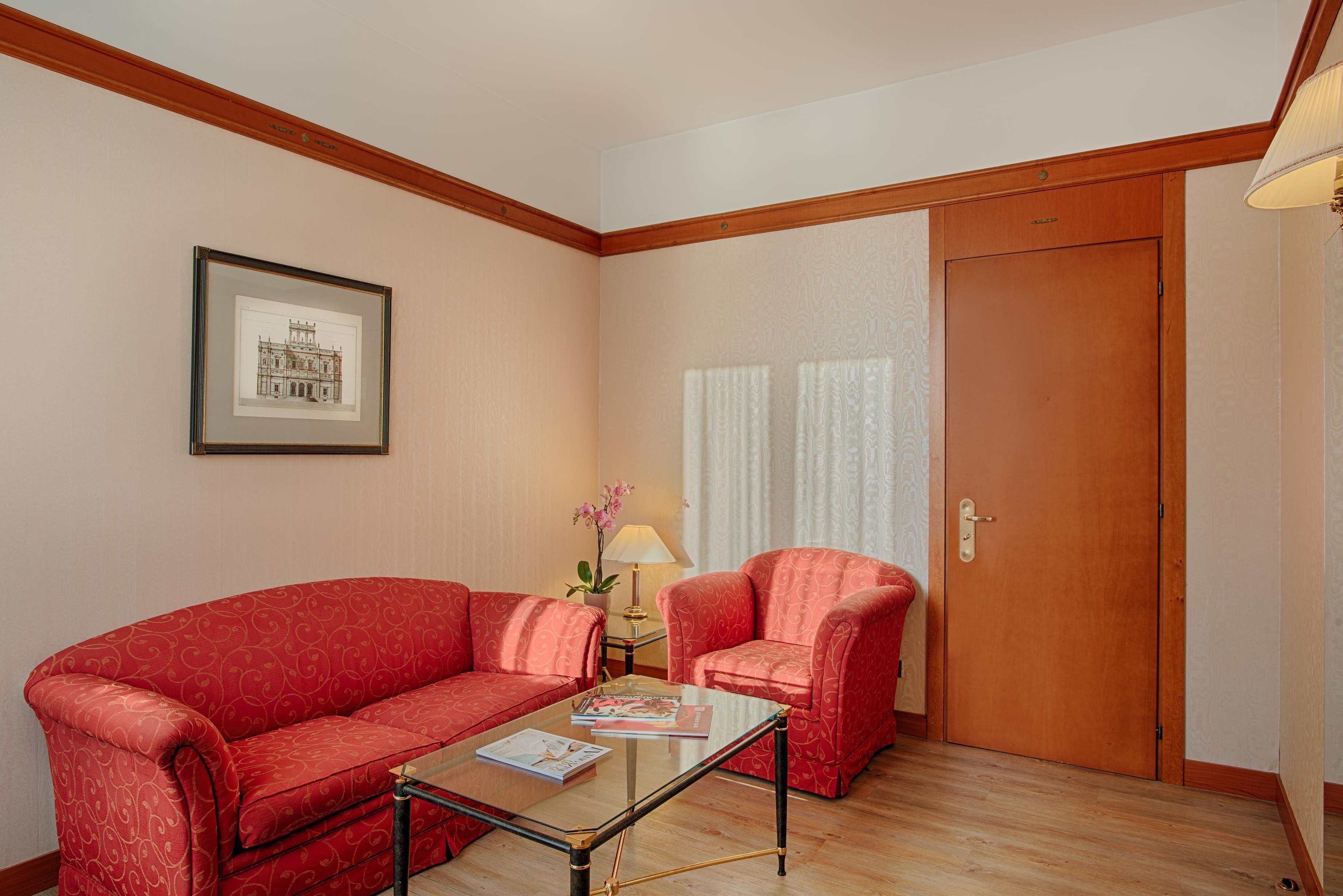 A room with a red sofa, a glass coffee table, a framed picture on the wall, a lamp, and a door.